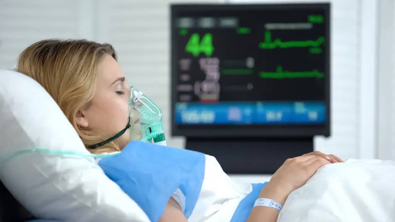 Kobieta w masce tlenowej leży w łóżku szpitalnym, monitor pokazuje parametry życiowe. Czy to syndrom łazarza?