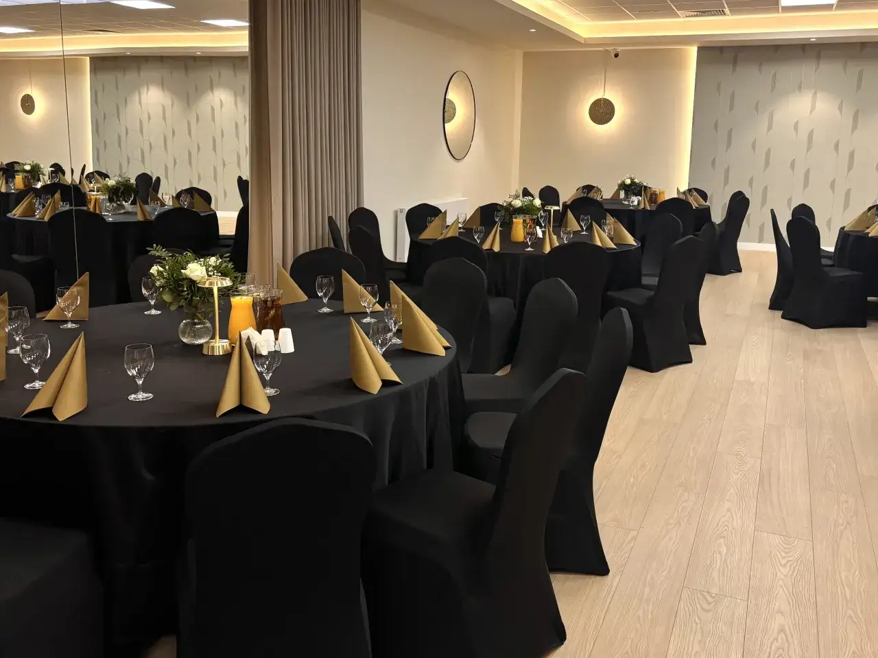 Elegancka sala bankietowa z czarnymi obrusami, złotymi serwetkami i kwiatami. Idealne miejsce na konsolację i uroczyste spotkanie.
