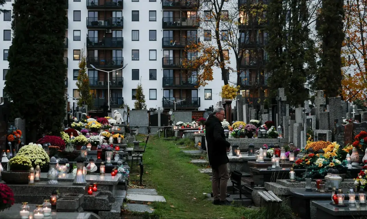 Cmentarz z nagrobkami i kwiatami, w tle blok mieszkalny. W oddali widać kolumbarium.