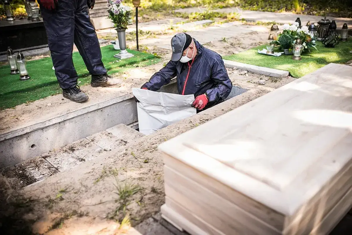 Pracownicy przygotowują ekshumację po 30 latach. Widać trumnę i koparkę.