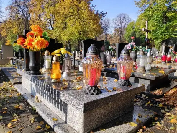 Jesienny dzień na cmentarzu. Na kamiennym, murowanym grobie palą się znicze, a obok stoją świeże kwiaty.